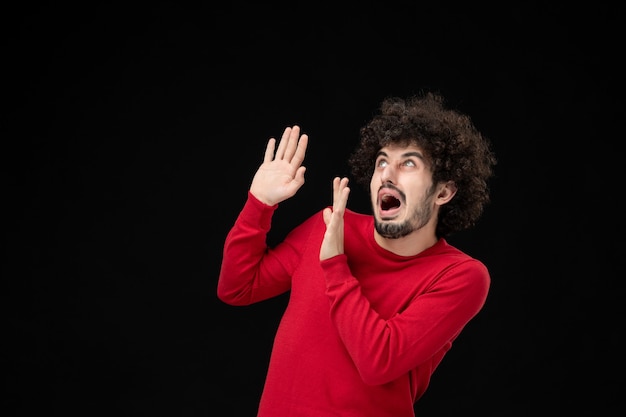 Front view of young male in red sweater on black wall