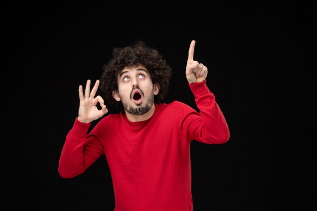 Front view of young male in red sweater on black wall