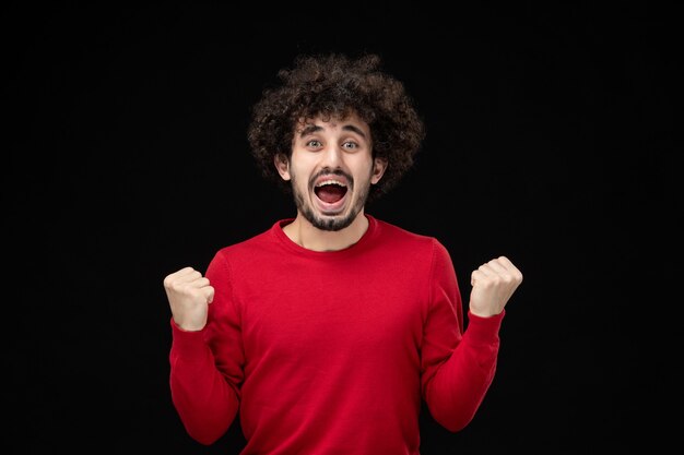 Front view of young male in red sweater on black wall