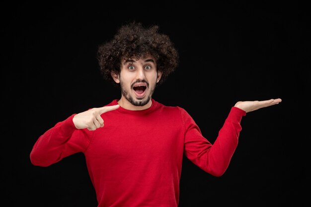 Front view of young male in red sweater on black wall