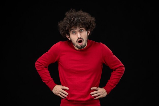 Front view of young male in red sweater on black wall