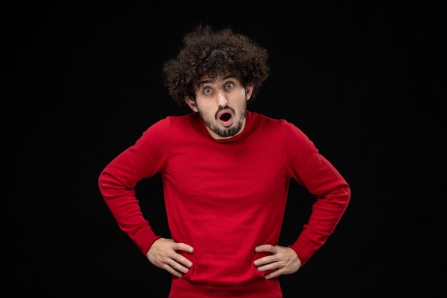 黒い壁に赤いセーターを着た若い男性の正面図