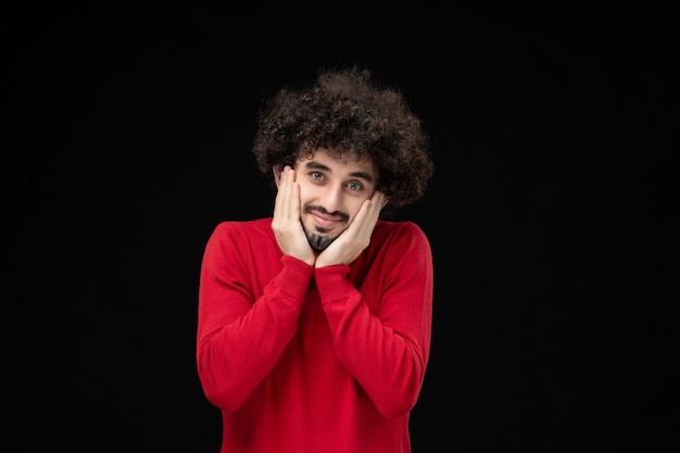 Front view of young male in red sweater on the black wall