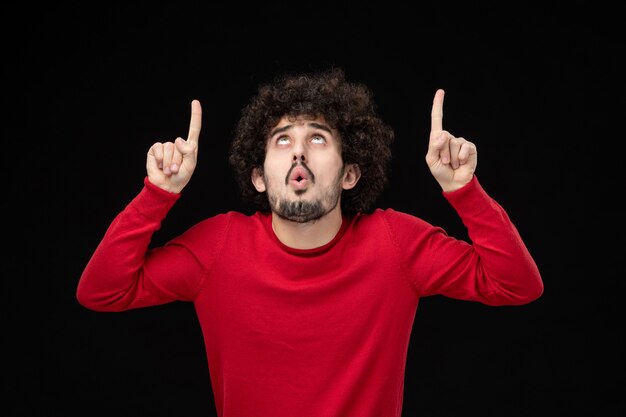 Front view of young male in red sweater on the black wall