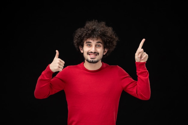 Front view of young male in red sweater on the black wall