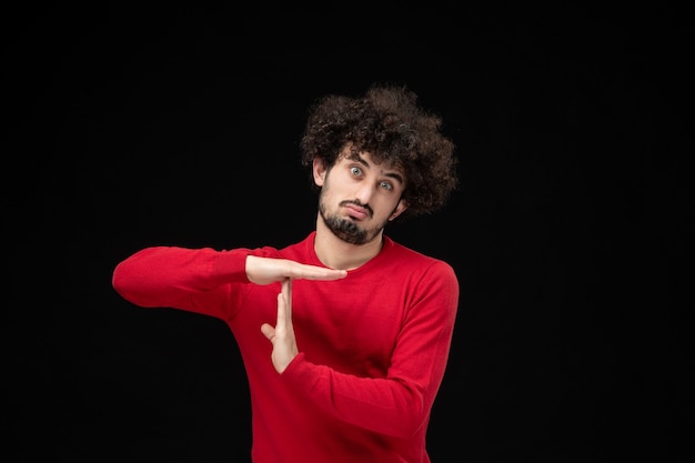 Front view of young male in red sweater showing t letter on black wall