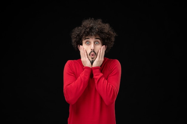 Front view of young male in red sweater surprised on the black wall