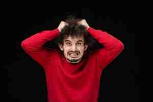 Free photo front view of young male in red sweater tearing his hair on black wall