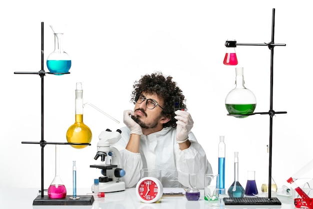 Front view young male scientist in special suit holding samples and thinking on white wall