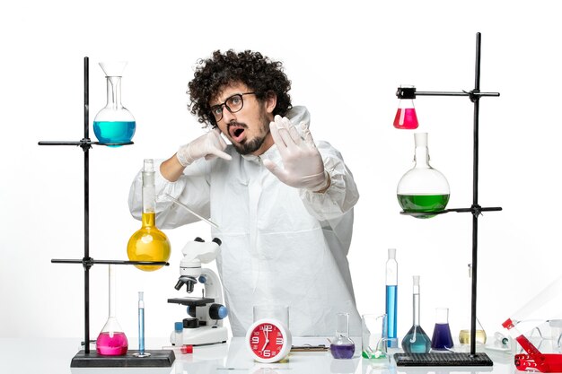 Front view young male scientist in special suit standing around table with solutions on white floor