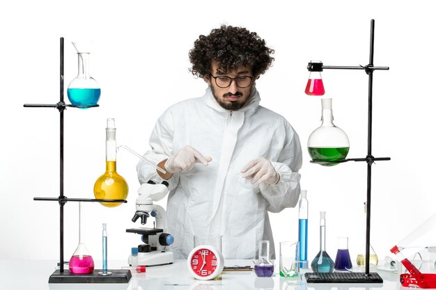 Вид спереди молодой ученый-мужчина в специальном костюме, стоящий за столом с растворами на белой стене