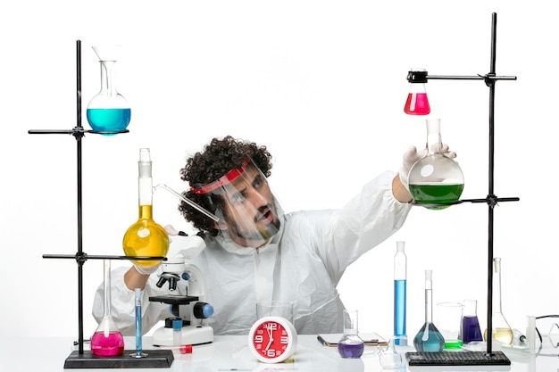 Вид спереди молодой ученый-мужчина в специальном костюме с защитным шлемом с помощью микроскопа на белой стене