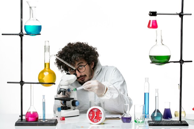 Вид спереди молодой ученый-мужчина в специальном костюме, работающий с инъекцией на белой стене