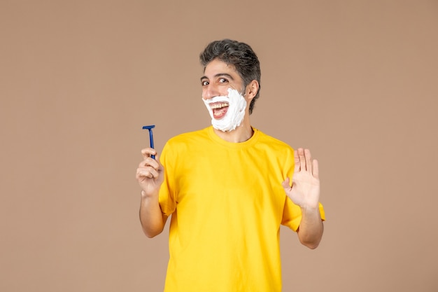 front view young male shaving his foamed face on pink background