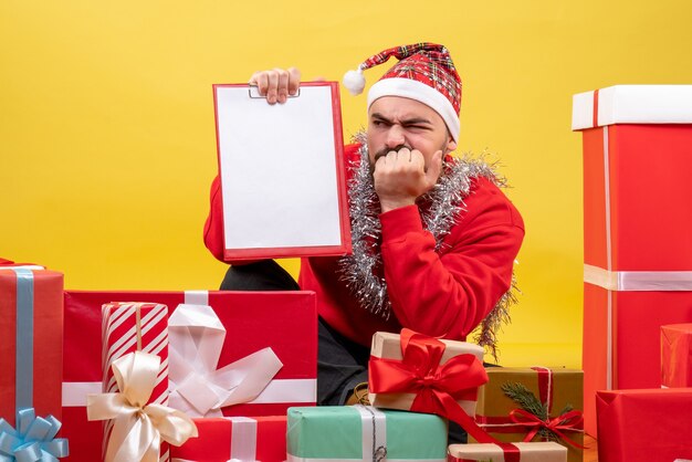 正面図黄色の背景にメモとクリスマスプレゼントの周りに座っている若い男性