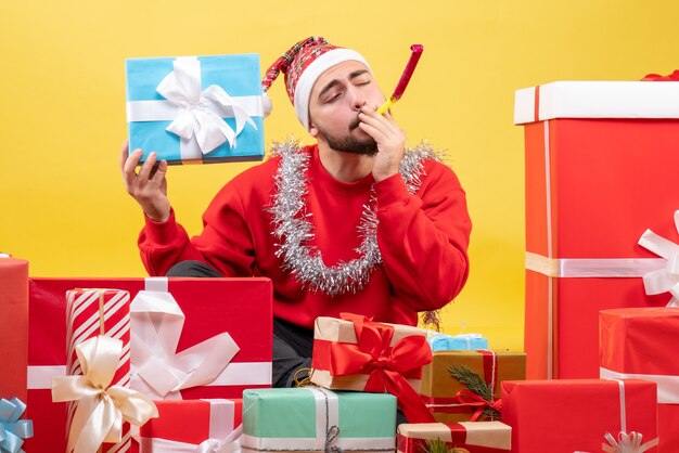 Вид спереди молодой мужчина сидит вокруг рождественских подарков на желтом фоне