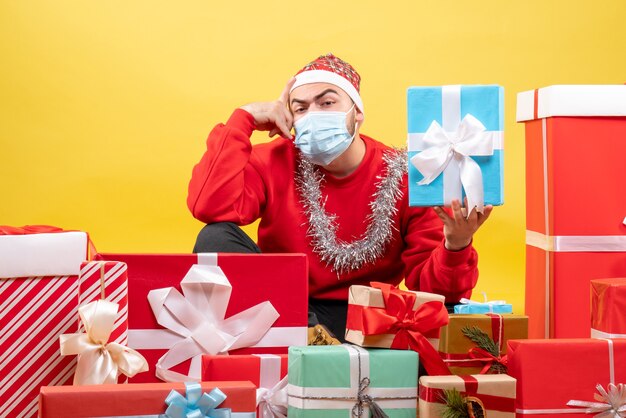 Front view young male sitting around christmas presents on a yellow background