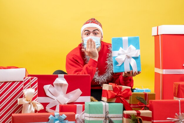 黄色の背景にクリスマスプレゼントの周りに座っている正面図若い男性