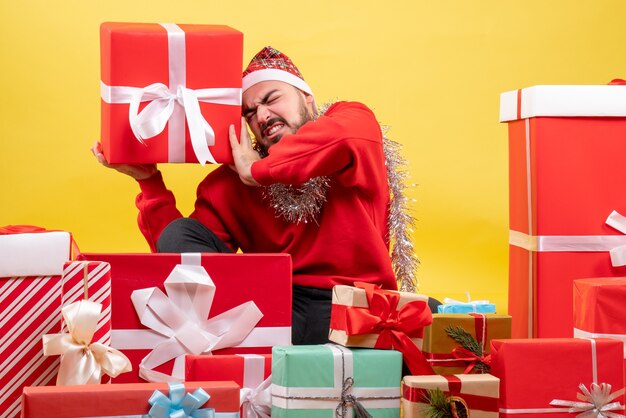 黄色の背景にクリスマスプレゼントの周りに座っている正面図若い男性
