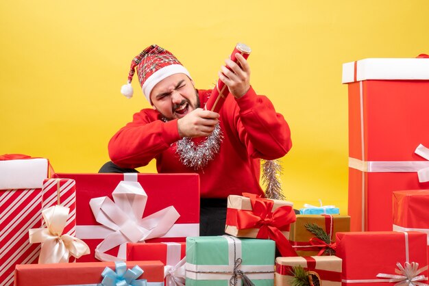 黄色の背景にクリスマスプレゼントの周りに座っている正面図若い男性