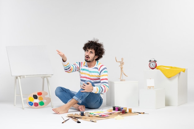 Front view of young male sitting around paints and drawings on a white wall