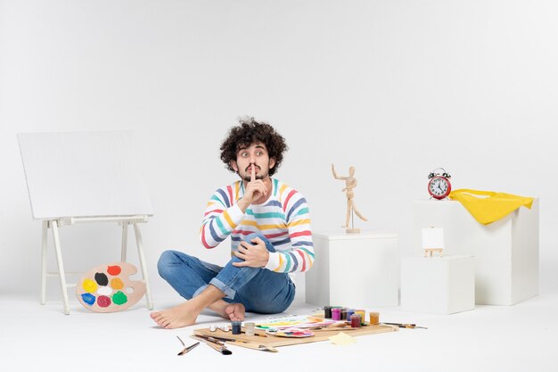 Front view of young male sitting around paints and drawings on a white wall