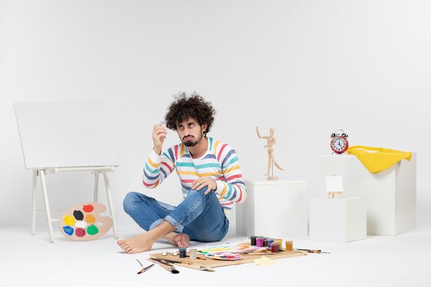 흰 벽에 페인트와 그림 주위에 앉아 젊은 남성의 전면 보기
