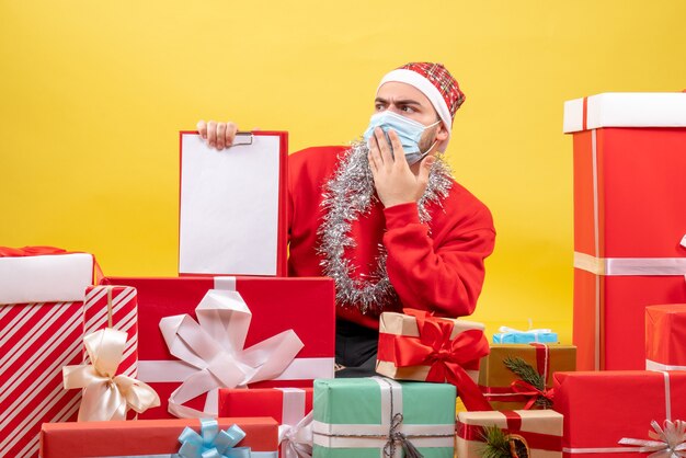 Front view young male sitting around presents in mask with note on a yellow background