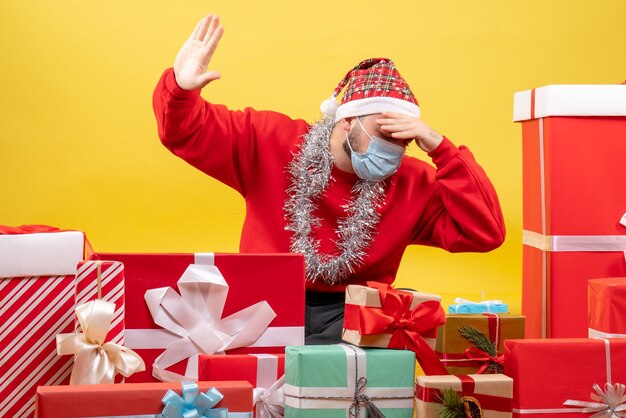 Front view young male sitting around presents in mask on a yellow background