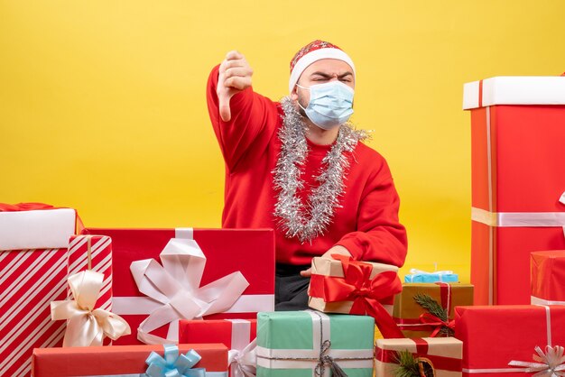 Front view young male sitting around presents in mask on the yellow background