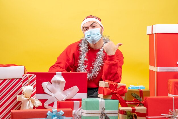 Front view young male sitting around presents in mask on yellow background