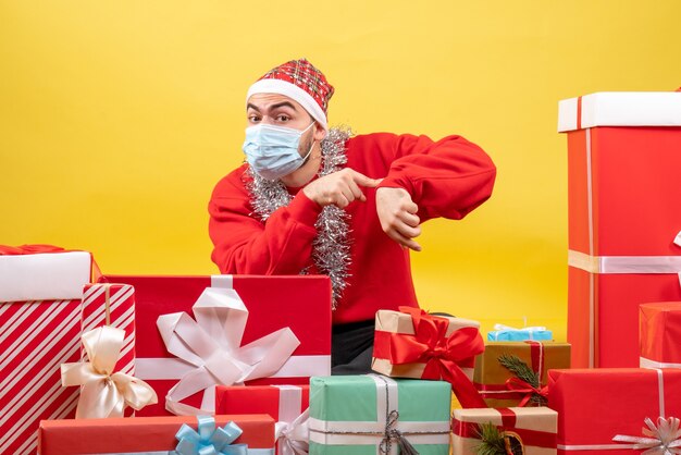 Front view young male sitting around presents in mask on yellow background