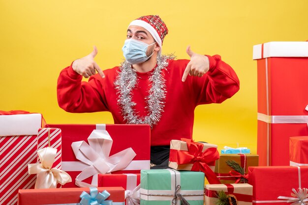 Front view young male sitting around presents in mask on yellow background