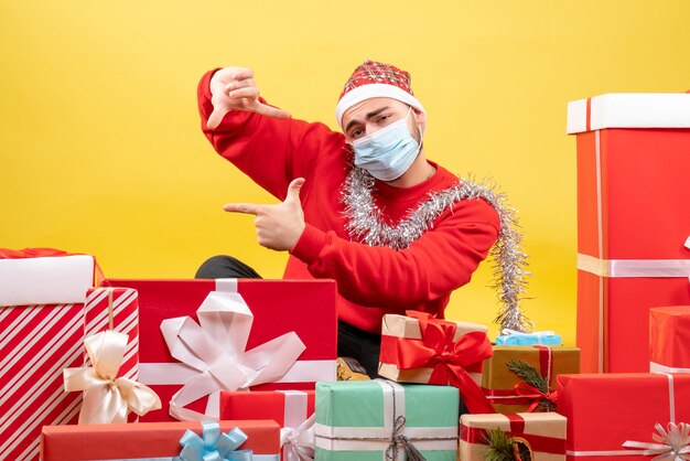 Front view young male sitting around presents in sterile mask on a yellow background