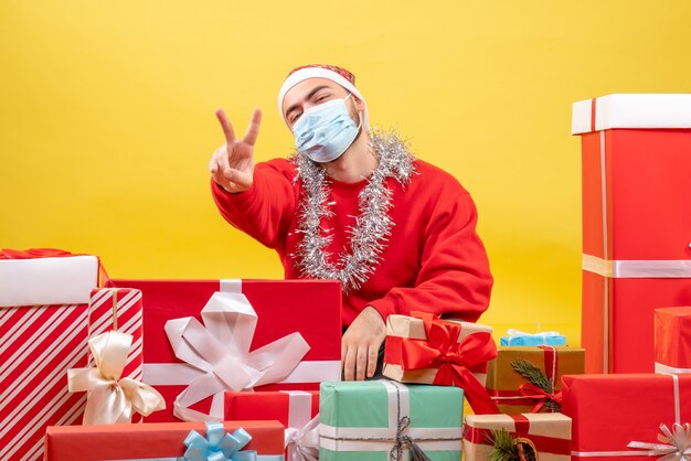 Front view young male sitting around presents in sterile mask on yellow background