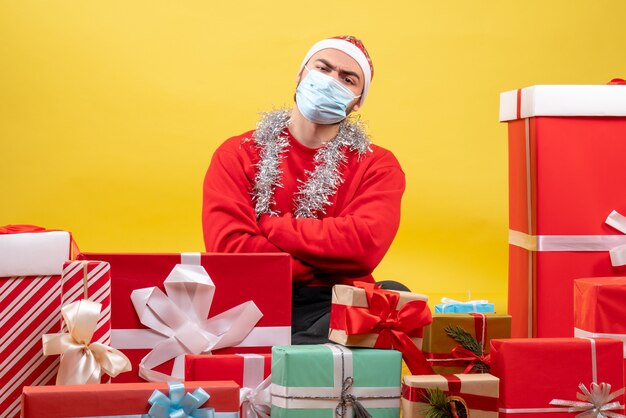 Front view young male sitting around presents in sterile mask on yellow background