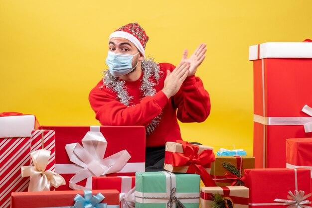 Front view young male sitting around presents in sterile mask on yellow background