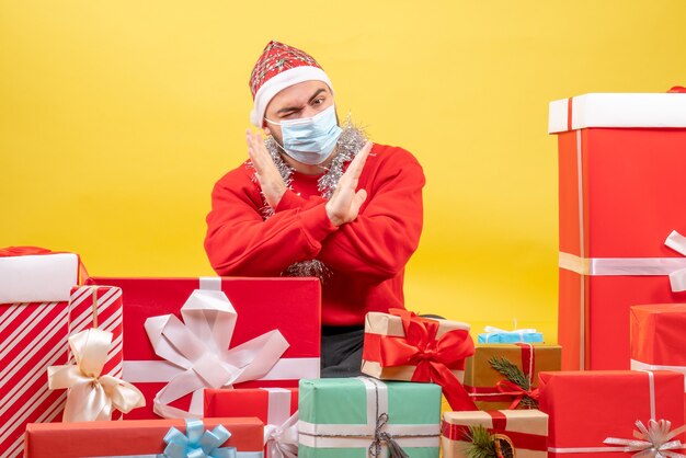 Front view young male sitting around presents in sterile mask on yellow desk