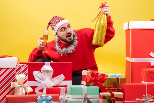 Front view young male sitting around presents with champagne on a yellow background