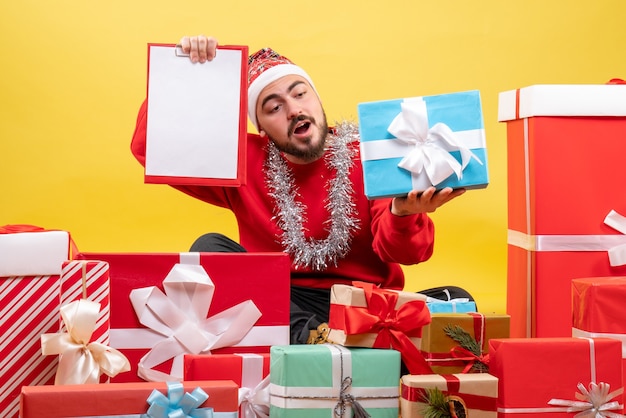 Front view young male sitting around presents with note on the yellow background