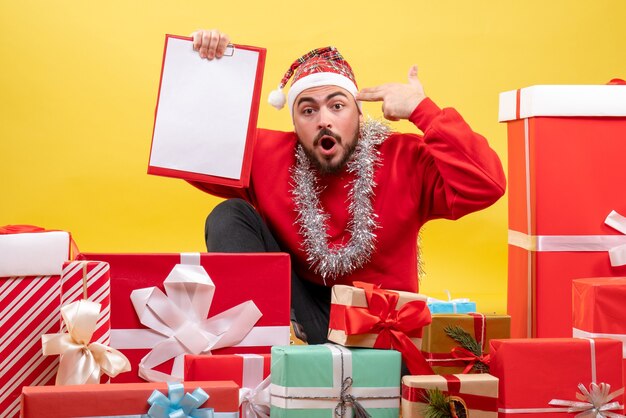 Front view young male sitting around presents with note on yellow background