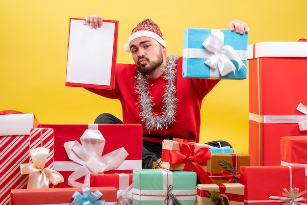 Front view young male sitting around presents with note on yellow background