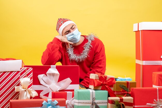 Front view young male sitting around presents on a yellow background