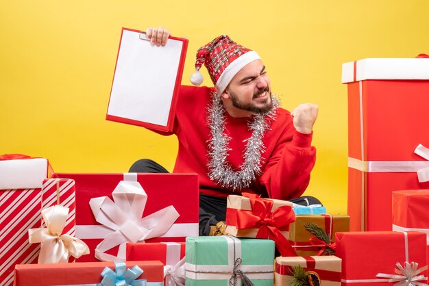 Front view young male sitting around presents on a yellow background