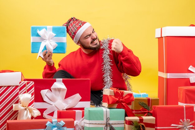 Front view young male sitting around presents on yellow background