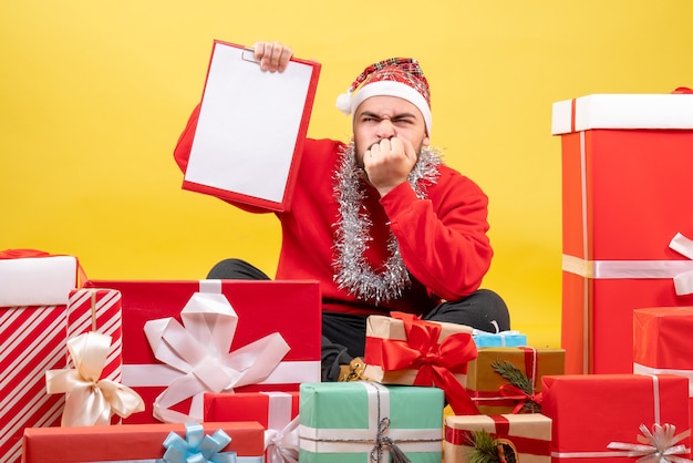 Front view young male sitting around presents on yellow background