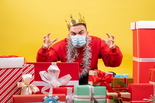 Front view young male sitting around xmas presents in mask on yellow background