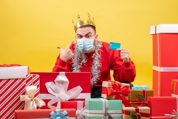 Front view young male sitting around xmas presents in mask on yellow background