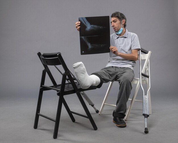 正面図若い男性が足を骨折して座って、灰色の壁にX線を保持している薬ねじれ男性の痛み足足が壊れている
