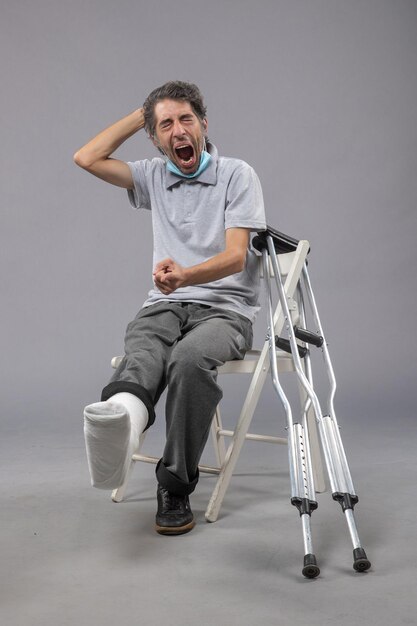 Front view young male sitting with broken foot and tied bandage on grey desk pain foot twist male accident